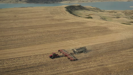 Farm-Tractor-Seeding-Slowly-Moving-On-Fields-Near-Serene-Lake-In-Saskatchewan,-Canada