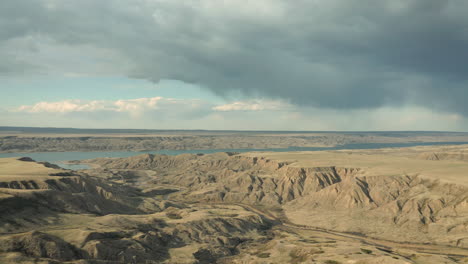 Clouded-Sky-Over-Vast-Erosion-Cliffs-With-Agricultural-Farmland-near-Lake-Diefenbaker,---Aerial-Drone-Shot