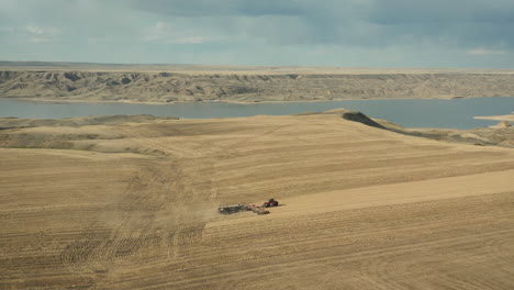 Farm-Seeding-In-Saskatchewan,-Canada-With-Blue-Lake-Background-Against-Gloomy-Sky