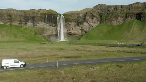 White-car-drives-on-rural-road-with-Seljalandsfoss-waterfall-in-background