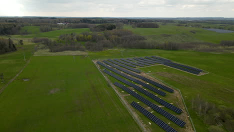 Aerial-backwards-shot-of-powerful-eco-friendly-solar-energy-farm-surrounded-by-rural-agricultural-fields