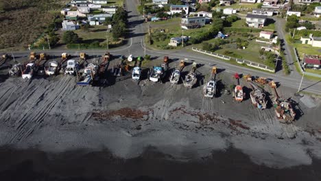Flying-along-a-line-of-boats-parked-on-a-beach-in-Ngawi,-New-Zealand
