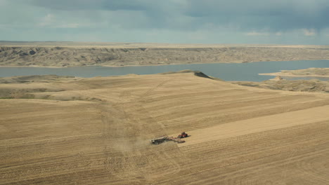 Golden-rural-landscape-of-Saskatchewan-with-tractor-seeding-field,-aerial