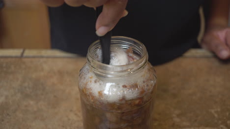 Raisins-soaking-in-a-canning-jar-for-a-homemade-vinegar-recipe---stirring-them-until-they-foam