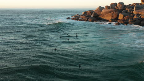 Surfers-relaxing-in-the-sea-and-watching-the-sunset-in-Llandudno,-Cape-Town,-South-Africa
