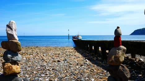 Colourful-rocks-arrangement-balanced-on-sunny-Llandudno-beach-seaside-shoreline-dolly-right-alongside-pier