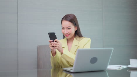Businesswoman-in-a-yellow-classic-suit-sitting-in-office-and-typing-with-both-hands-message-in-mobile-phone