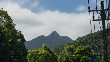 Timelapse-De-4k-De-Cumbre-Montañosa-Con-Nubes-Formándose-Sobre-El-Pico-Contra-Un-Cielo-Azul-En-La-Isla-De-Koh-Chang-En-Tailandia-Con-Postes-Eléctricos-Al-Costado-De-La-Carretera