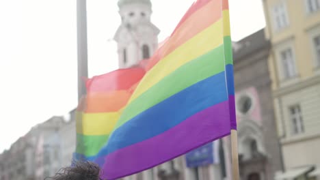 Zeitlupe-Einer-Regenbogen-lgbtq-Flagge,-Die-Während-Einer-Pride-Demonstration-In-Einem-Städtischen-Hintergrund-Mit-Häusern-Im-Verschwommenen-Hintergrund-In-Der-Luft-Weht
