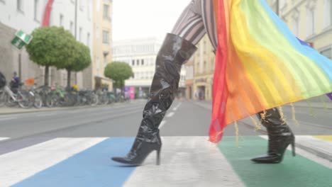 Close-up-of-legs-of-a-transgnder-in-long-black-heels-crossing-a-rainbow-lgbtq-cross-walk-in-an-urban-city-environment,-wearing-a-rainbow-scarf