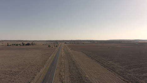 Aerial-wide-shot-rising-up-vertically-to-reveal-more-of-the-drought-affected-landscape,-as-a-white-vehicle-speeds-past-on-the-road