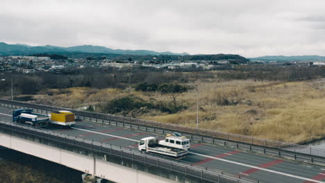 Coches-Que-Viajan-En-El-Puente-Mutsumi-Con-Vistas-Al-Estanque-De-Ballenas-Y-Al-Prado-Ribereño-En-Tokio,-Japón