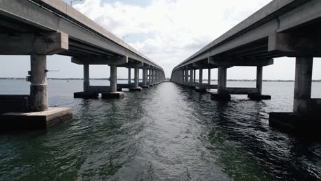 Drone-shot-flying-under-bridge-over-water-on-a-sunny-Florida-day