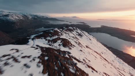 Fast-flying-over-snowy-mountain-ridge-during-colorful-sunset-in-Norway