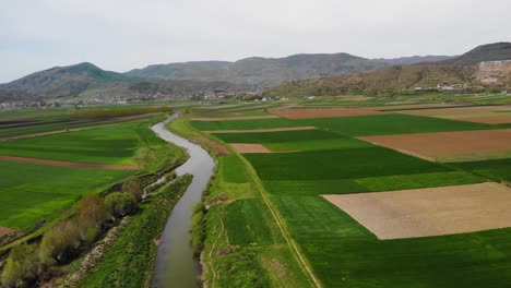 Agricultural-parcels-of-crops-and-river-streaming-from-mountains,-Aerial-view