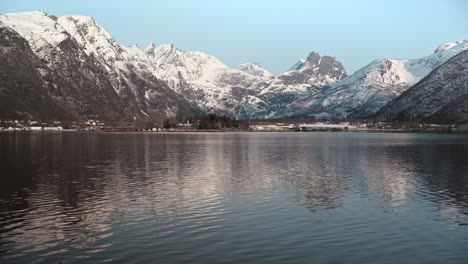 Stunning-shot-taken-across-a-still-lake,-with-huge-snow-covered-mountains-surrounding-the-lake