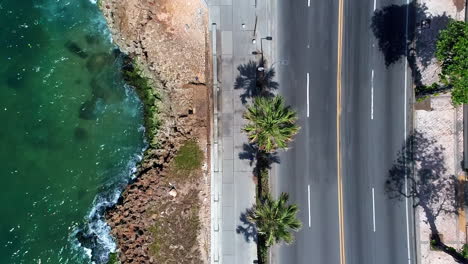 Vista-Aérea-De-Arriba-Hacia-Abajo-Del-Malecón-De-Santo-Domingo-Frente-Al-Mar-Con-Gente-Caminando-Y-Montando-En-Bicicleta
