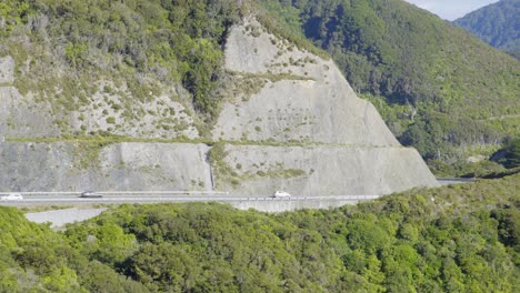 A-long-shot-of-cars-driving-on-a-mountain-road-next-to-a-large-road-cutting