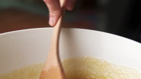 Macro-shot-of-hand-mixing-delicious-food-in-bowl-with-wooden-spatula
