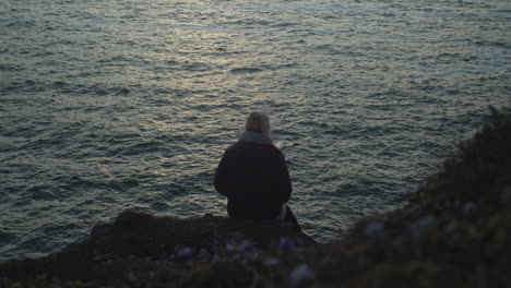 Woman-Sitting-At-The-Edge-Of-A-Hill-Overlooking-The-Sea-In-Sunset---medium-shot