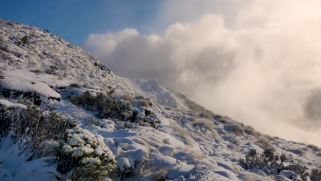 Panning-shot-of-lighting-cloudscape-hiding-behind-snowy-mountain-during-Kepler-Track-Hike-in-New-Zealand