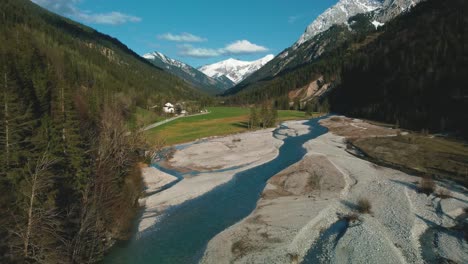 Aerial-of-a-scenic-mountain-river-with-fresh-blue-water-in-the-Bavarian-Austrian-alps-by-afternoon-sunshine,-flowing-down-a-gravel-riverbed-along-trees,-forests-and-hills-seen-by-drone-flight-from-up