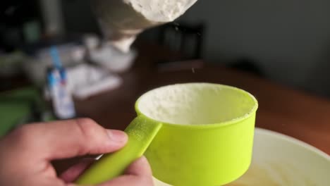 close-up-of-pouring-flour-into-light-green-plastic-measuring-cup