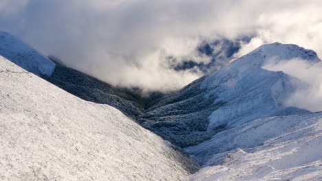 Luftaufnahmen-Von-Oben-Nach-Unten-Einer-Gigantischen-Schneebedeckten-Berglandschaft,-Umgeben-Von-Wolken-Im-Sonnenlicht
