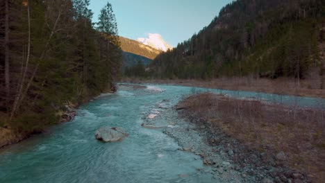 Aerial-flight-along-a-scenic-mountain-river-with-fresh-blue-water-in-the-Bavarian-Austrian-alps-by-sunshine-,-flowing-down-a-riverbed-along-trees,-rocks,-forest-and-hills-seen-from-above-by-drone