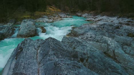Low-aerial-drone-flight-along-a-scenic-and-idyllic-mountain-river-waterfall-canyon-with-fresh-blue-water-in-the-Bavarian-Austrian-alps,-flowing-down-a-beautiful-riverbed-along-trees,-forest-and-rocks