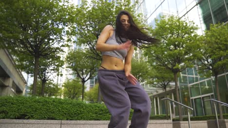 Positive-Gesunde-Vegane-Tänzerin-Mit-Schönem-Körper-Und-Haut,-Die-Frei-Mit-Grünem-Hintergrund-Voller-Bäume-Und-Gebäude-In-Zeitlupe-Tanzt