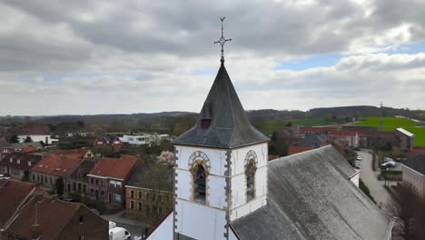 Aerial-drone-counter-rotation-around-church-clock-with-Belgian-hills-in-the-background