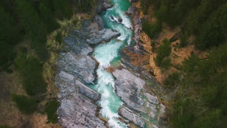 Aerial-flight-above-a-scenic-and-idyllic-mountain-river-waterfall-canyon-with-fresh-blue-water-in-the-Bavarian-Austrian-alps,-flowing-down-a-beautiful-riverbed-along-trees,-forest-and-rocks-from-above
