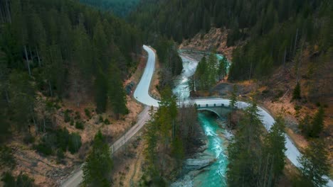 Aerial-flight-above-a-scenic-mountain-river-with-fresh-blue-water-in-the-Bavarian-Austrian-alps-by-afternoon-sunshine,-flowing-down-a-riverbed-along-trees,-forests,-a-street-and-hills-seen-by-drone