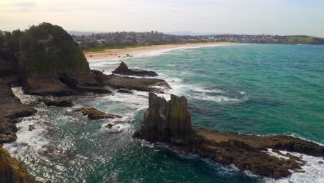 View-of-Cathedral-Rocks-near-Kiama-in-New-South-Wales,-Australia,-with-Jones-Beach-in-the-distance---aerial-shot