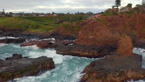 Foamy-Waves-Crashing-Against-The-Orange-And-Brown-Cliffs-At-Cathedral-Rocks-Near-Coastal-Town-In-Kiama-Downs,-New-South-Wales,-Australia---aerial-shot