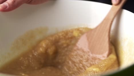 Closeup-of-mixing-raw-cookie-dough-using-wooden-spoon-in-bowl
