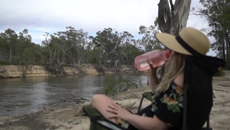 Woman-sitting-on-camping-chair-drinking-water-on-hot-Australian-day
