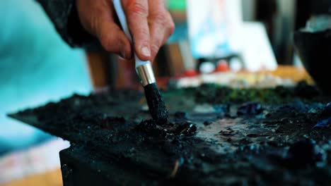 Artist-Painter-getting-the-black-paint-from-his-palette-to-his-brush-to-start-painting