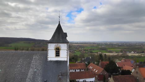 Aerial-drone-rotating-around-church-clock-with-Belgian-hills-in-the-background