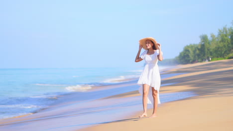 Mujer-Feliz-Con-Vestido-Blanco-De-Verano-Y-Sombrero-De-Paja-Caminando-Descalzo-Por-La-Playa-En-El-Fondo-De-Las-Mareas-Marinas,-Día-Soleado-En-La-Playa-De-La-Isla-Tropical