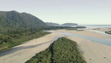 Aerial-flyby-shot-of-an-untouched-beach-by-a-forested-cliff-in-west-coast-New-Zealand