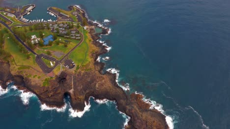 Top-Down-View-Of-Sandstone-Headland-With-White-Lighthouse-and-Breakwater-Stone-Wall-Protecting-Wollongong-Harbour-And-Marina-In-NSW,-Australia---aerial-shot