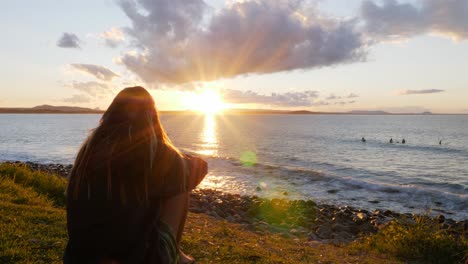 Mädchen-Sitzt-Und-Bewundert-Die-Goldene-Sonnenuntergangskulisse-Im-Ozean---Sonnenuntergang-Im-Noosa-Nationalpark-In-Queensland,-Australien