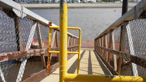 Yellow-painted-railings-on-seafront-boardwalk-jetty-slope-leading-to-calm-sea-waves-dolly-right