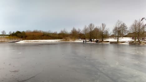 Panoramic-shot-of-a-frozen-pond-and-children-ice-skating