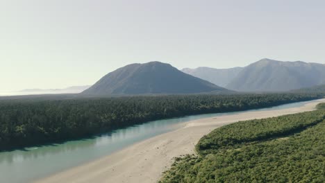 Aerial-panning-left-to-right-shot-of-a-river-with-a-mountainous-range-in-the-background-in-the-west-coast-of-New-Zealand