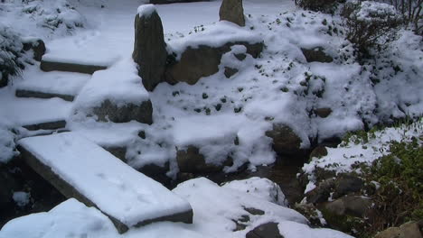 Slow-zoom-in-on-snow-covered-footbridge-and-Japanese-garden