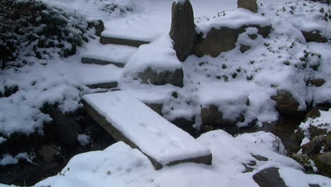 Slow-zoom-out-on-snow-covered-footbridge-and-Japanese-garden