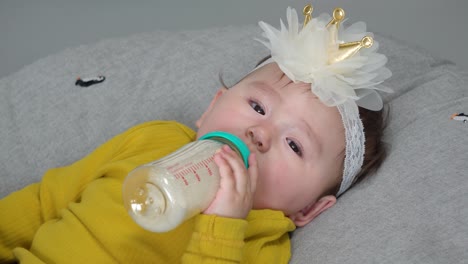 Pretty-11-month-baby-girl-drinks-formula-milk-from-bottle-lying-on-donut-cushion